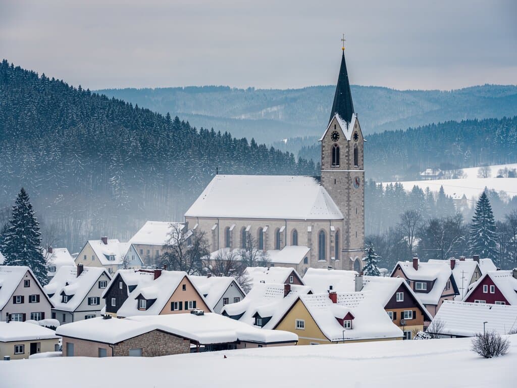 Snow-covered Vogtland village with church steeple and pine-forested hills